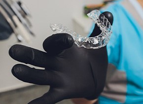 Dentist with black gloves holding clear aligner