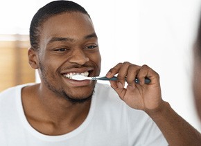 Man smiling while brushing his teeth in bathroom