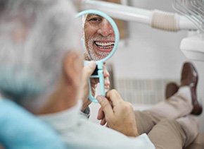 mature man smiling in mirror at dentist appointment