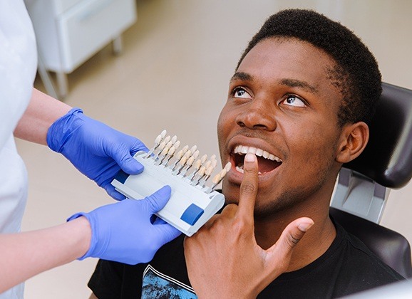 Man pointing to smile compared with tooth shade chart