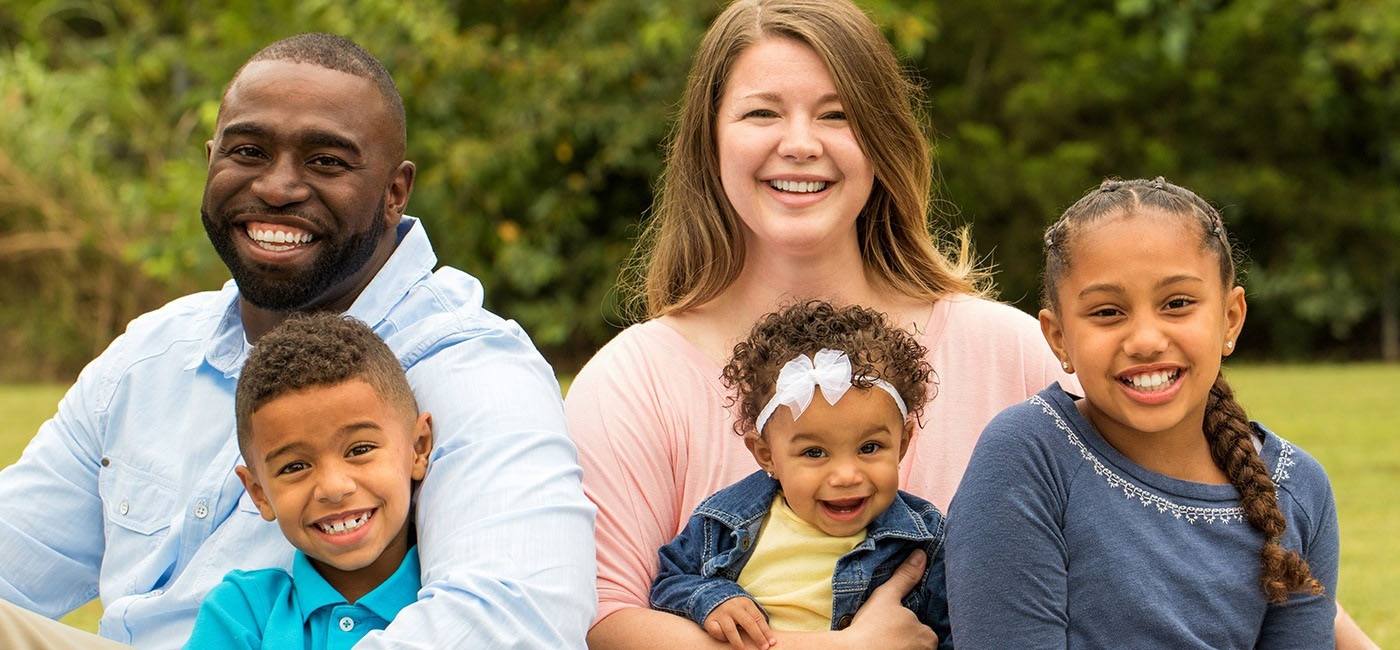 Mother father and three children smiling together outdoors