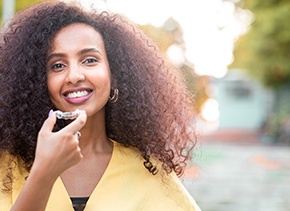 Woman in yellow shirt smiling while holding Invisalign aligner