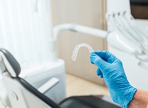 Orthodontist holding aligner with blue glove in office