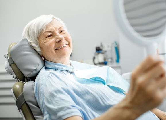 Woman looking at smile after dental bridge placement